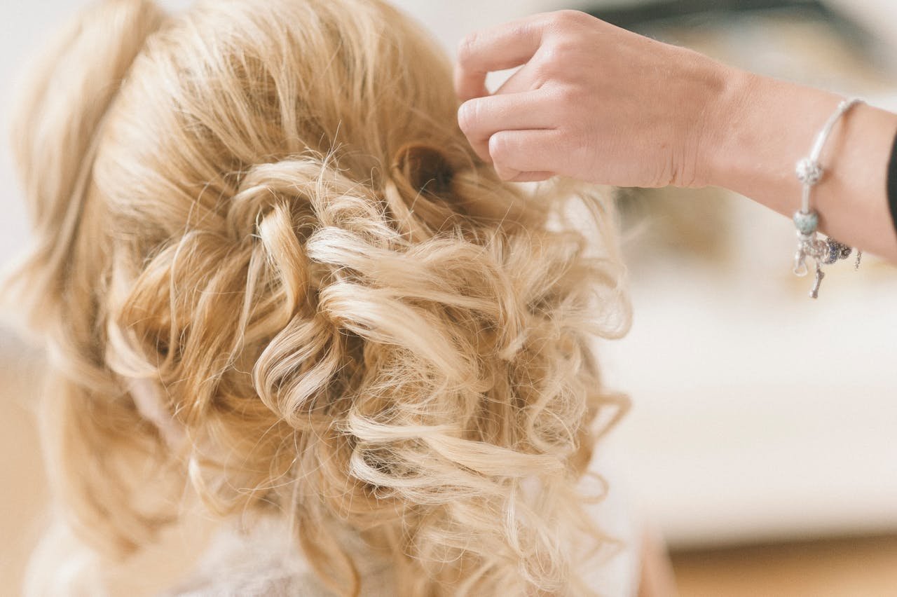 A professional hairstylist creates a blonde bridal updo for a wedding.