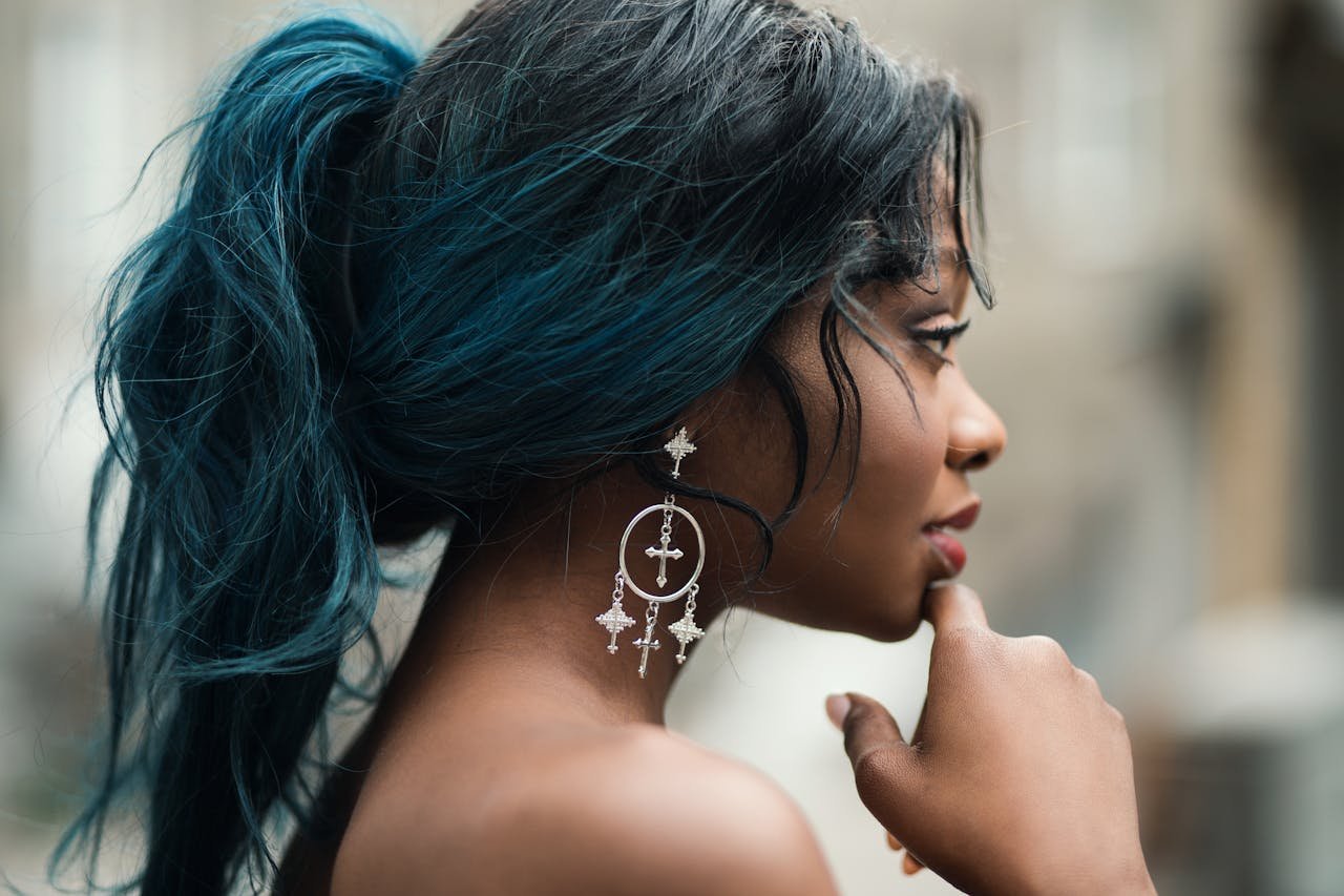 Side profile of a woman with blue hair and decorative earrings, captured in natural light outdoors.